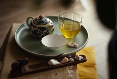 Still life photo of patterned clay teapot, clear glass pitcher, tea cup with fresh brewed oolong tea on tray in ceremony room. Soft light, wooden tea tray evoke calming mindful Chenese atmosphere.  clipart