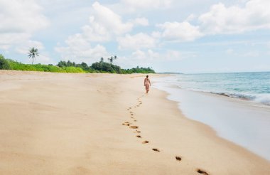 Young female dressed in light summer clothes walking barefoot leaving footprints on the sand on Indian ocean Tangalle lonely coconut trees beach on Sri Lanka island. Aerial top view drone shot. clipart