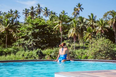 Mayo giymiş bir kadın sonsuz yüzme havuzunda dinleniyor ve Pinnawala Fil Yetimhanesi 'ndeki orman kıyılarıyla geniş kayalık nehir manzarasını seyrediyor..