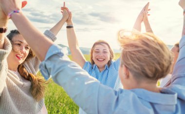 Gün batımında yeşil tepenin yanından geçerken el ele tutuşan ve gülümseyen dört kadının portresi. Kadınların dostluğu, ilişkileri ve mutluluk konsepti imajı.