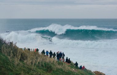 Uluslararası sörfçüler Praia do Norte 'de Nazare, Farol da Nazar, Portekiz' de büyük Atlantik okyanus dalgalarının tadını çıkaran insanlar en yüksek sörf rekorunun kırıldığı yerde