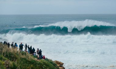 Uluslararası sörfçüler Praia do Norte 'de Nazare, Farol da Nazar, Portekiz' de büyük Atlantik okyanus dalgalarının tadını çıkaran insanlar en yüksek sörf rekorunun kırıldığı yerde