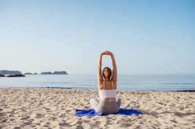 Sakin bir kadın oturur, derin nefes alır, sıkı egzersizler yapar ve sabahın erken saatlerinde sakin deniz dalgalarıyla kumlu sahilde meditasyon yapar. Akıl sağlığı, dinlenen insanlar, seyahat konsepti.