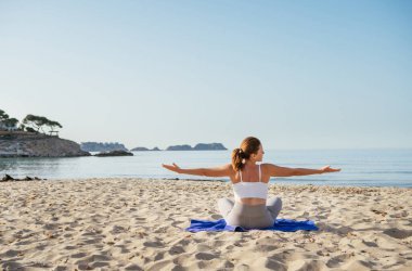 Sakin bir kadın oturur, derin nefes alır, sıkı egzersizler yapar ve sabahın erken saatlerinde sakin deniz dalgalarıyla kumlu sahilde meditasyon yapar. Akıl sağlığı, dinlenen insanlar, seyahat konsepti.