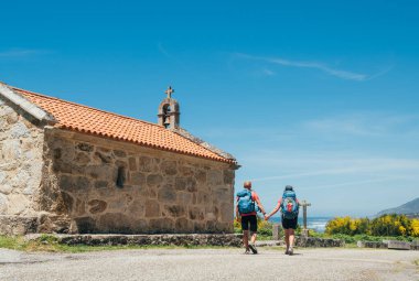 Camino Portuguese Yolu 'ndaki eski kilisenin yanında sırt çantalı birkaç hacı el ele yürüyorlar. Ünlü Camino de Santiago' da ilham verici bir yürüyüş yapıyorlar. Seyahat, hac, yaşam tarzı, mimari