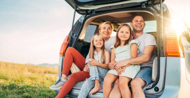 Otomobil kazasında küçük kızları olan mutlu genç bir çiftin portresi. Gülüyorlar, gülüyorlar ve sohbet ediyorlar. Aile değerleri, seyahat kavramı.