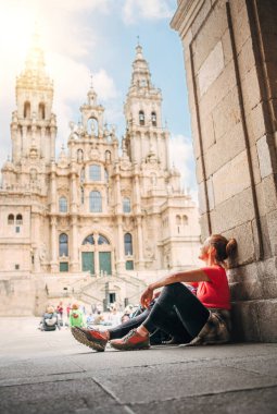 Santiago de Compostela Katedrali ünlü Camino de Santiago ile birlikte İspanya 'nın Santiago de Compostela kentindeki Obradoiro meydanında oturan neşeli orta yaşlı gezgin kadın.