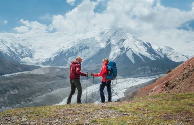 Sırt çantalı sırt çantalı çiftler, Lenin zirvesine çıkarken arka planda dağ zirveleri olan yürüyüş direkleri. Aşırı aktif insanlar, yüksek irtifa Pamir alan dağcılık konsepti