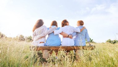 Açık hava yürüyüşü sırasında çayır bankında otururken kucaklaşmak, hafif yaz kıyafetleri giymiş dört gülümseyen kadın için zararlı. Kadınların dostluğu, ilişkileri ve mutluluk konsepti imajı.