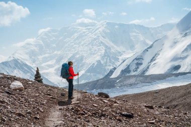 Lenin zirvesi boyunca sırt çantası ve yürüyüş direkleri olan yalnız dağcı kadın dağ zirveleri ve buzulların keyfini çıkarıyor. Aşırı aktif insanlar, yüksek rakımlı dağcılık konsepti.