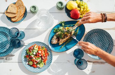 Mangalda ızgara ızgara, beyaz ahşap masada sebze salatası ve meyveli bir kadın tarafından servis ediliyor. Sağlıklı deniz ürünleri yemeği, taze yemek, açık hava yemek konsepti fotoğrafı..