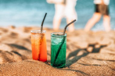 Kumda buzlu ve samanlı renkli içecekler. Arkaplanda insanlar ve deniz.