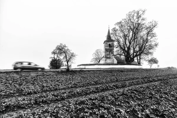 車の動きがぼやけている農村部の国とスロバキアのルドバ村の古いゴシック様式の教会 白黒写真 — ストック写真