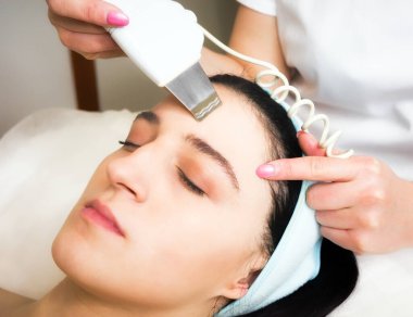 Güzellik uzmanı güzellik salonunda genç bir kıza yüz bakımı ve yaşlanma karşıtı tedavi uyguluyor..