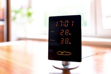 Hot summer day. High temperatures showing on display of home meteo station. Sun shine through window.