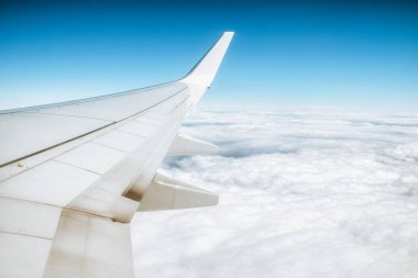 Gökyüzündeki uçak penceresinden ve altındaki bulutlardan bak. Kanatçıklar uçağın kanadında