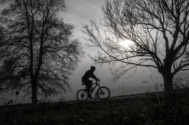 Adam sisli sonbahar sabahında yokuş yukarı bisiklet sürüyor. Ürkütücü karanlık hava