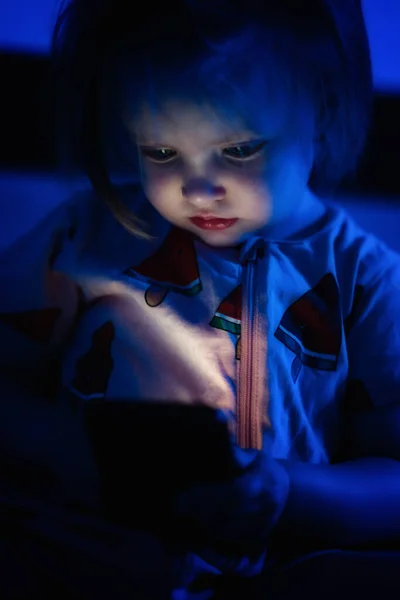 Toddler girl playing with smarthphone in bed at night.