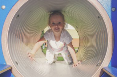 Gülümseyen mutlu küçük kız oyun sahasındaki tünelde oynuyor..