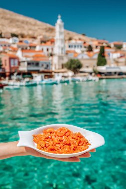 Beyaz tabakta karidesler arka planda deniz ile el ele tutuşuyor..