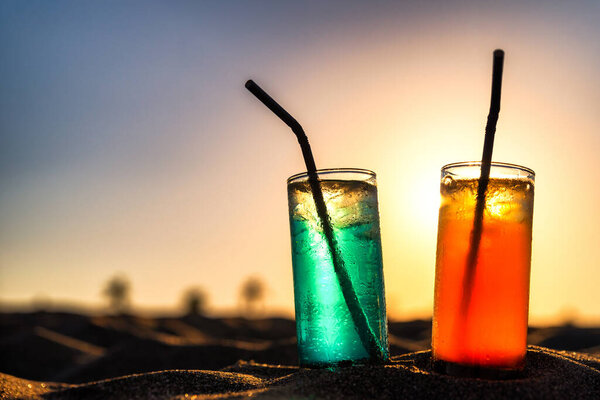 Concept of luxury tropical vacation. Classic cocktails in sand and colorful sky