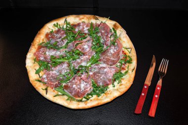 Prosciutto, roka ve peynirli pizza restoranda yenmeye hazır.