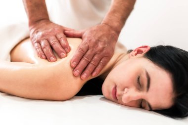 Masör, beyaz arka planda masaj masasında yatan genç bir kadının sırt ve omuzlarına masaj yapıyor. Masaj spa tedavisi kavramı..
