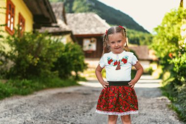 Kırsal kesimde geleneksel Vlkolinec köyünde, Slovakya 'da ahşap kulübelerle poz veren dört yaşında mutlu küçük bir kız çocuğu.