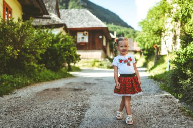 Kırsal kesimde geleneksel Vlkolinec köyünde, Slovakya 'da ahşap kulübelerle poz veren dört yaşında mutlu küçük bir kız çocuğu.
