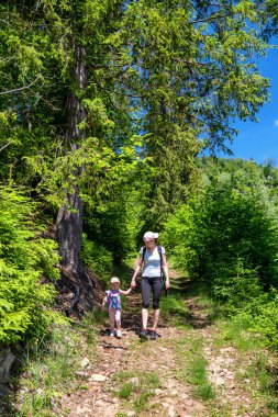 Anne ve bebek yeşil ormanda yürüyorlar.
