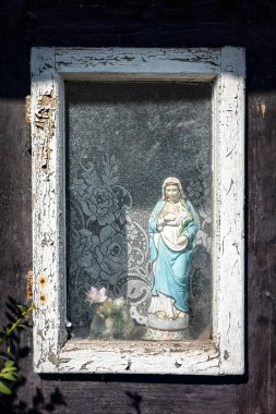 Eski ahşap kulübenin camındaki Meryem Ana heykeli.
