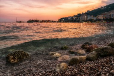 Çakıl taşlı plajda kayalar ve Karadağ 'ın Budva kentinde güzel turuncu gün batımı gökyüzü.