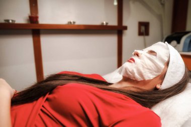 Güzeller güzeli kadın güzellik salonunda yüz bakımı yaptırıyor ve kafasında yüz maskesi var..