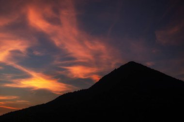 Tepenin siluetinin üzerindeki bulutlarda renkli turuncu ışık.