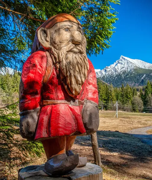 Ormanda yüksek tepeleri ve dağları olan tahta bir goblin heykeli. Slovakya 'daki High Tatras dağlarında Pea Krivan