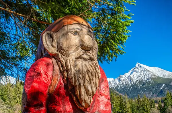 Ormanda yüksek tepeleri ve dağları olan tahta bir goblin heykeli. Slovakya 'daki High Tatras dağlarında Pea Krivan