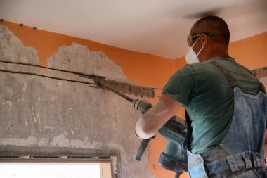 Kaya matkabıyla çalışan işçiler eski dairenin yeniden inşası üzerinde çalışıyorlar. Kelimeler duvarda yazılı..