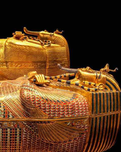 Vertical close-up photo of the golden coffin of pharaoh Tutankhamun with intricate colored inlays and protective gods, showcasing ancient Egyptian art and burial craftsmanship on black background.