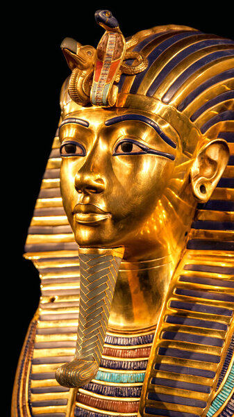 Vertical close up of Tutankhamuns iconic golden funerary mask with brilliant blue inlays, uraeus cobra and vulture emblems, symbolizing power and protection in ancient Egyptian burial art.