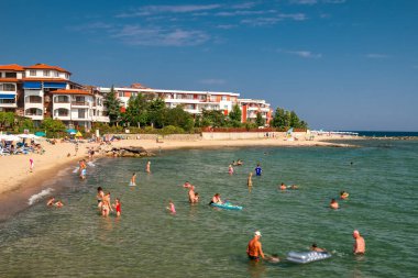 Bulgaristan 'ın Elenite kenti - 17 Temmuz 2025: Yaz tatilinin tadını çıkaran turistler, Fort Noks Ayrıcalıklı tatil beldesi binalarıyla Karadeniz' de kumsalda yüzüyorlar
