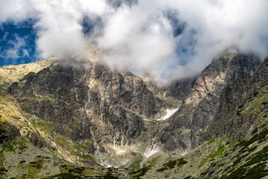 Slovakya 'nın yüksek Tatras kentindeki Lomnicky dik zirvesi, kısmen bulutlarla kaplı kayalık uçurumlar, kar yamaçlarında ve yamaçlarında dağlık yamaçlarda dağlık arazi ve yürüyüş varış noktalarında bulunan alp bitkileri,.