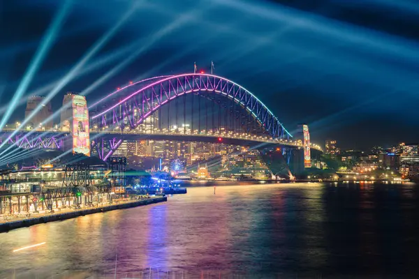 Liman köprüsü ve liman kenti silueti üzerinde renkli Sydney Lazer Gösterisi 3 Haziran 2025 'te Avustralya' da uzun pozlu bir fotoğrafla geceleyin çekildi.
