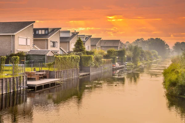 Homes on water edge in residential area in the Netherlands. Under orange sky.