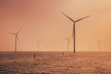 Denizdeki Offshore Wind çiftliği. IJsselmeer Gölü 'nde, bulutlu günbatımı gökyüzünün altında bir grup rüzgar türbini. Rüzgar enerjisi sürdürülebilirliğe doğru yeşil geçişte en ucuz elektrik formlarından biri haline geldi. Hollanda.