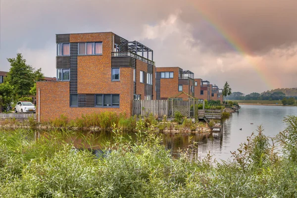 Homes on water edge in residential area in the Netherlands. Under cloudy sky with rainbow. Heerhugowaard, Netherlands.
