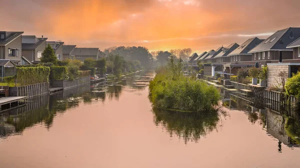 Homes on water edge in residential area in the Netherlands. Under orange sky.