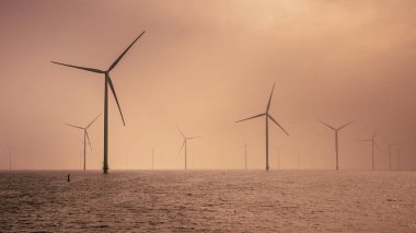 Denizdeki Offshore Wind çiftliği. IJsselmeer Gölü 'nde, bulutlu günbatımı gökyüzünün altında bir grup rüzgar türbini. Rüzgar enerjisi sürdürülebilirliğe doğru yeşil geçişte en ucuz elektrik formlarından biri haline geldi. Hollanda.