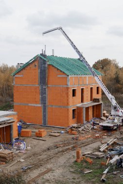 Turuncu tuğla ve betondan yapılmış üç katlı bir evin yapım süreci. Bir inşaat alanının penceresinden görüntüle.