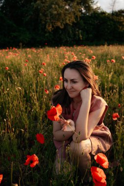 Gün batımında haşhaş tarlasında kahverengi doğal saçlı ve tozlu gül takım elbiseli genç bir kadın. Polonya 'da yaz, Varşova.