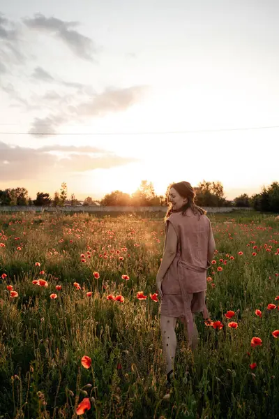 Gün batımında haşhaş tarlasında kahverengi doğal saçlı ve tozlu gül takım elbiseli genç bir kadın. Polonya 'da yaz, Varşova.